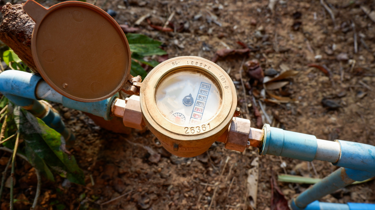 Outdoor water meter with its lid open, connected to blue pipes