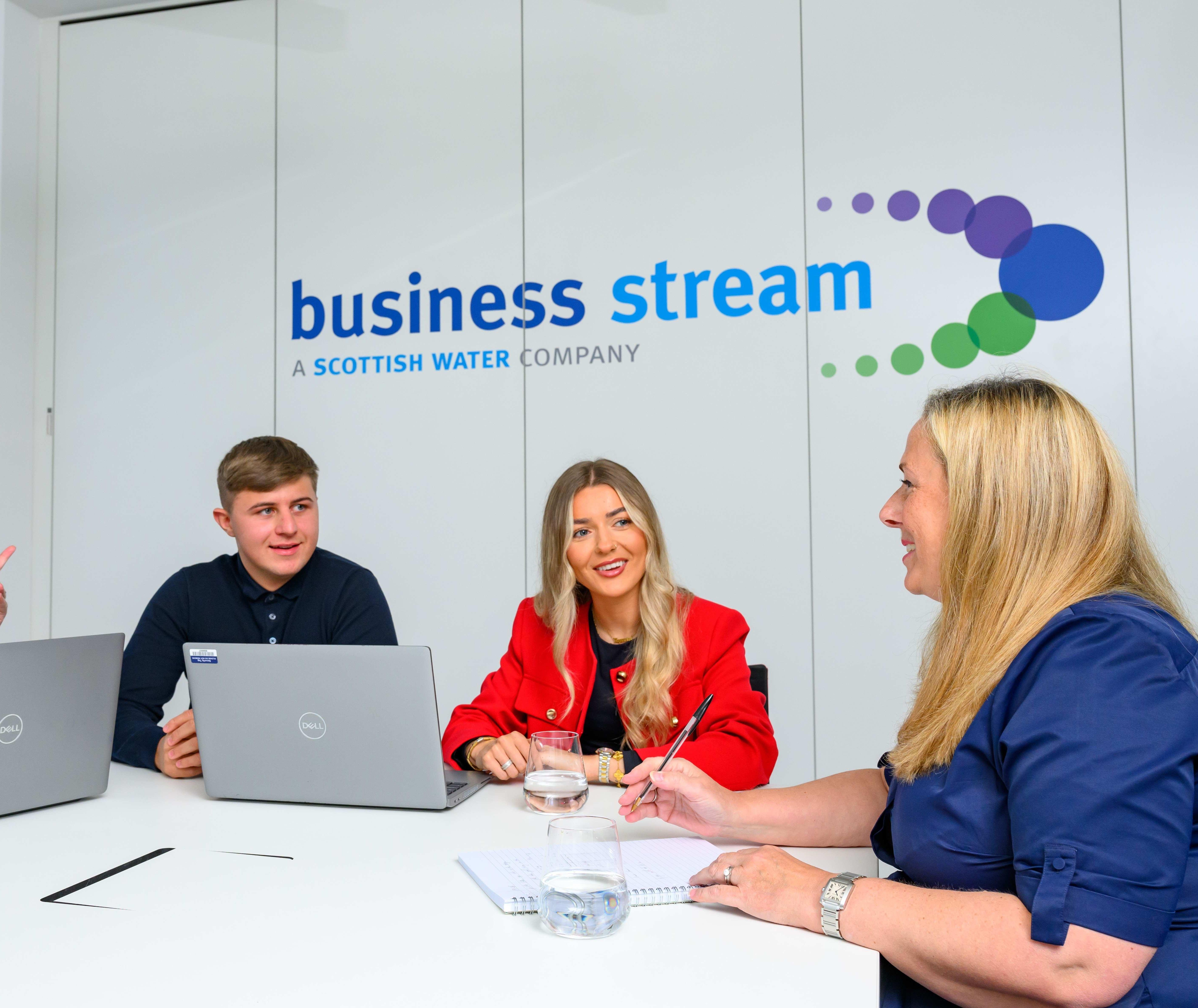 Three women and a man seated in a meeting room with Business Stream logo on wall behind