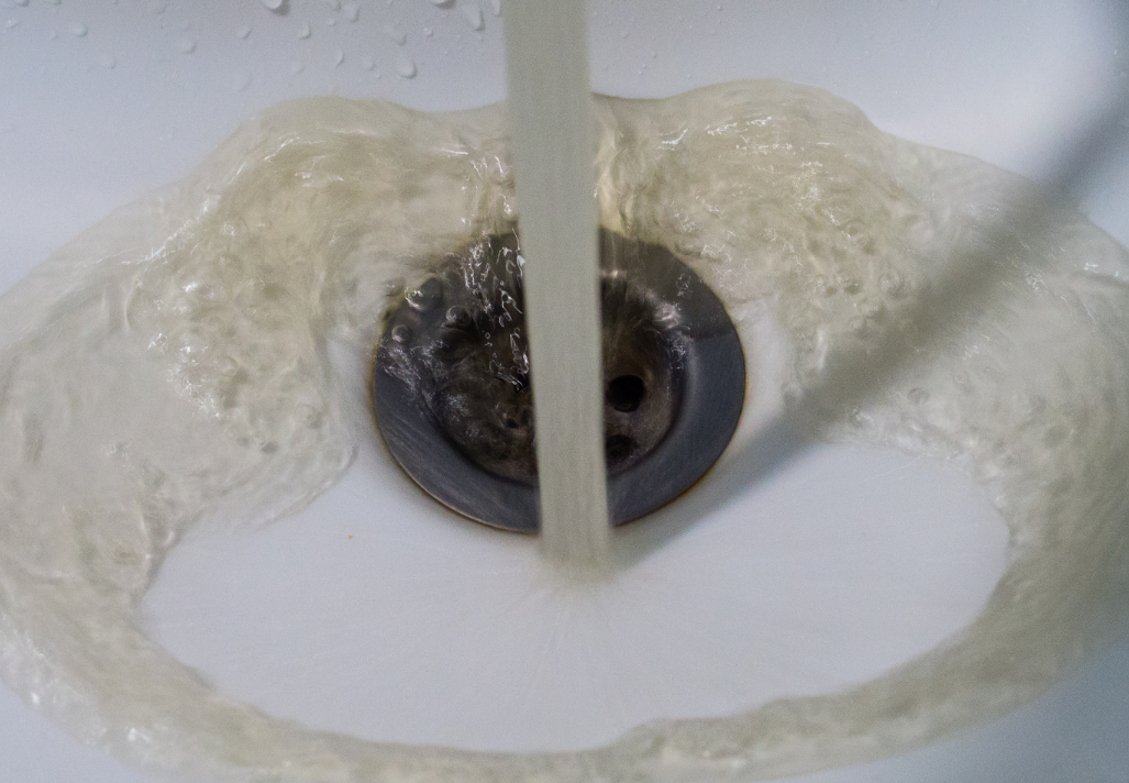 Discoloured water flowing from a tap into a white sink
