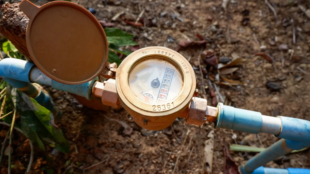 Outdoor water meter with its lid open, connected to blue pipes