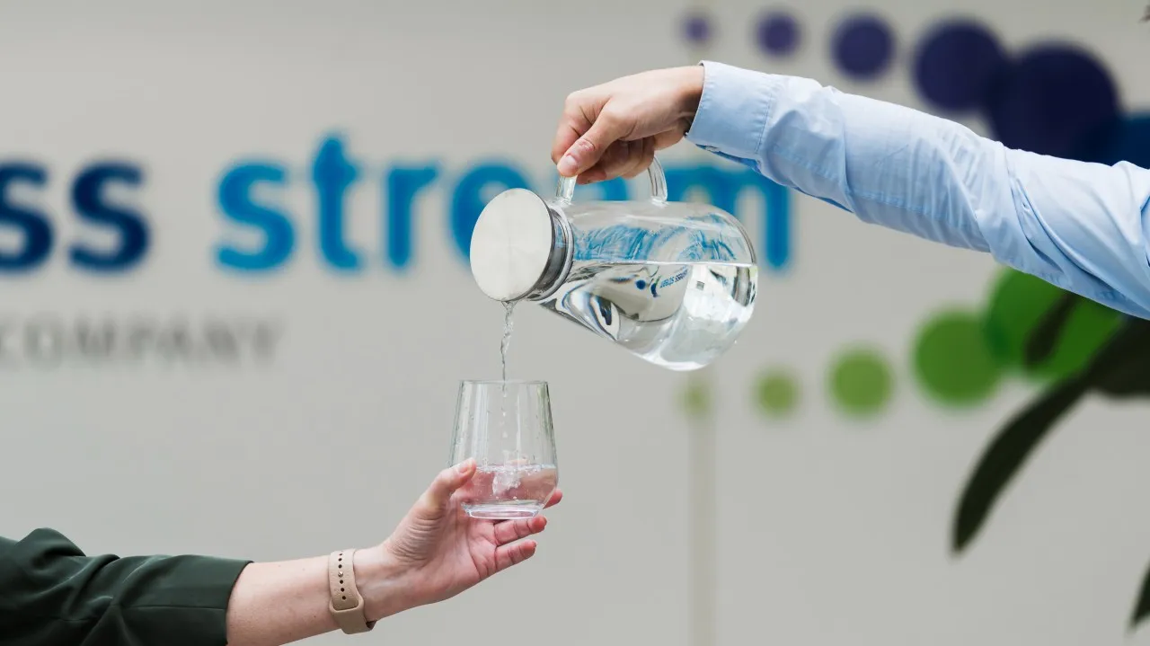 Water being poured from a glass jug into a glass held by another person