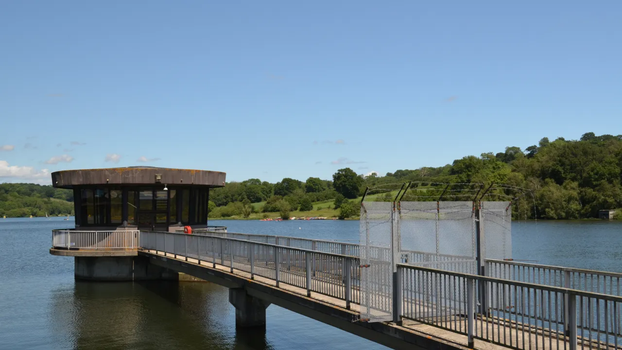 Walkway leading to a small building over a lake with trees and blue sky in the background