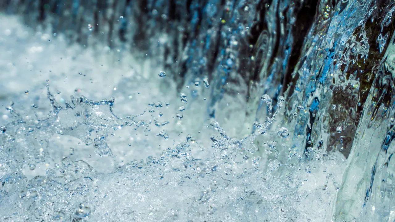 A close-up image of water cascading down a waterfall with splashes and droplets captured in mid-air. The water appears clear and blue.