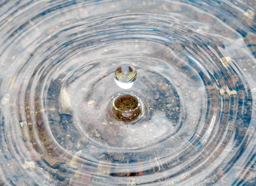 Water drop rising from a splash with pebbles visible below