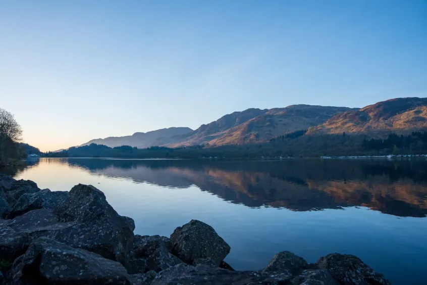 Loch Earn with still water, clear blue sky above and mountains in the background