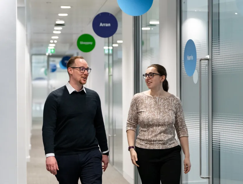 A man and a woman chatting as they walk along an office corridor