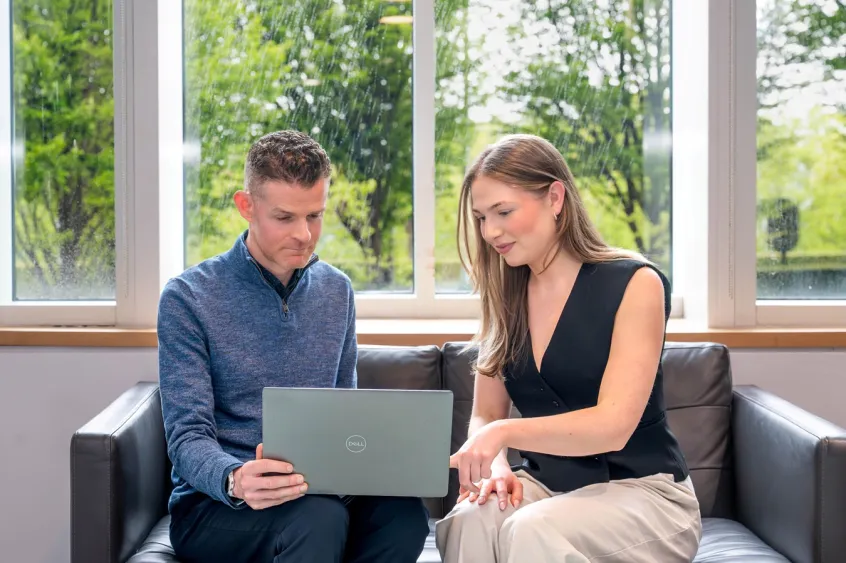 Woman explaining online billing to someone, while they both look at a laptop