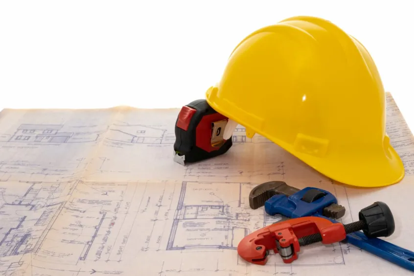Yellow hard hat, tape measure and other tools sitting on a construction plan