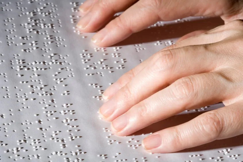 Hands right of shot reading braille text on white paper