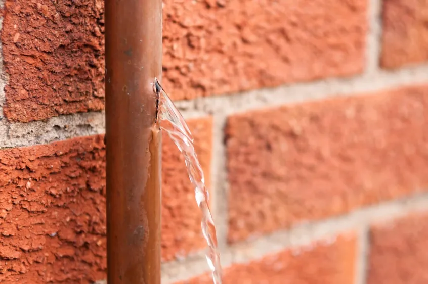 Leaking copper water pipe against a red brick wall