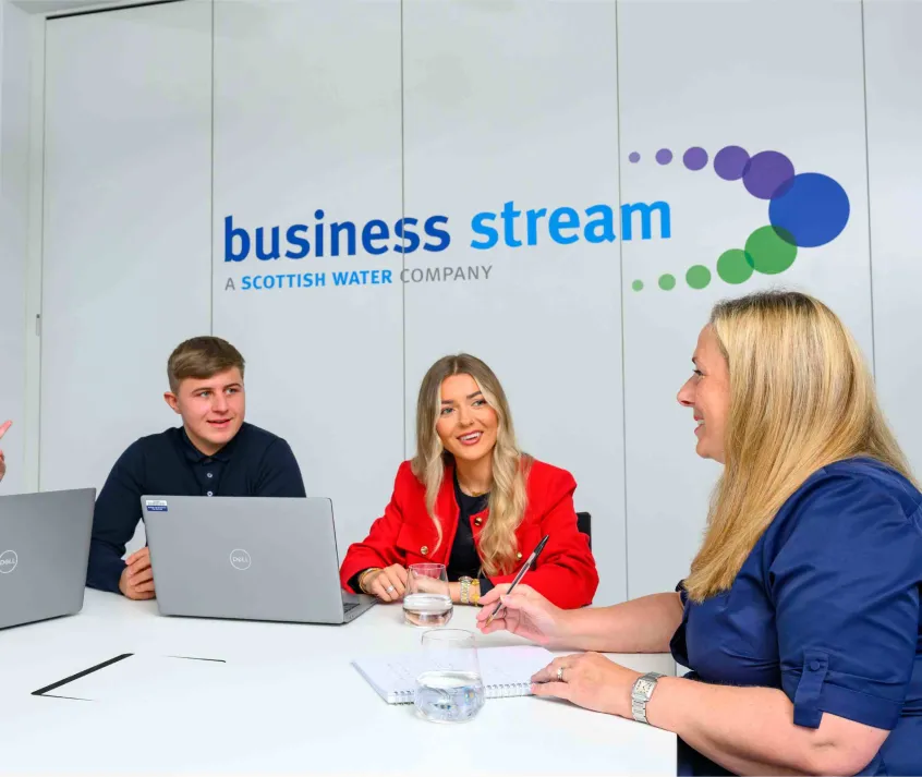 Three women and a man seated in a meeting room with Business Stream logo on wall behind