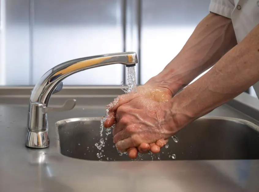 Man washing hands under running tap in commercial kitchen