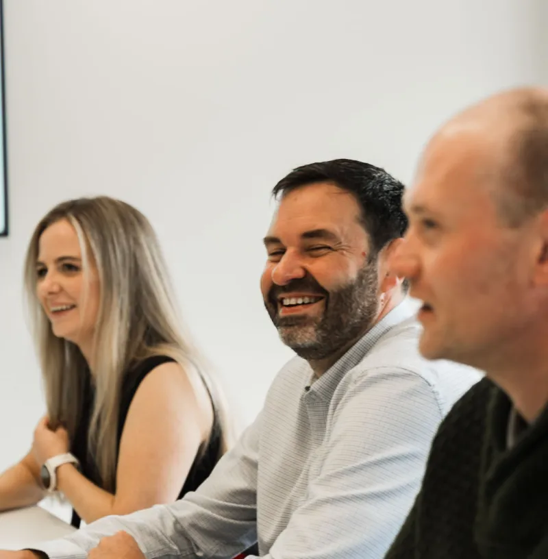 Tight in on woman and two men sitting side by side in a meeting room