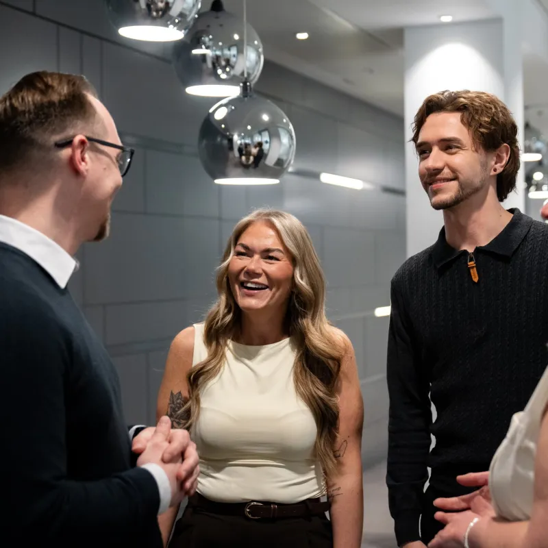 A woman and two men standing smiling and chatting against a dark grey background