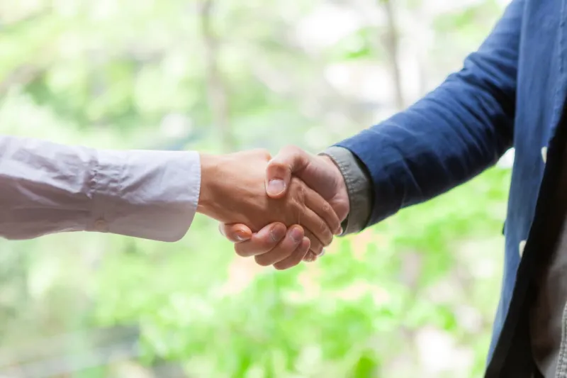 Close-up of woman and man shaking hands with greenery in background