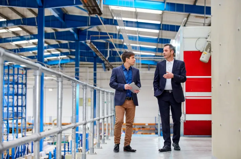 Two smartly dressed men talking as they walk through a large factory setting