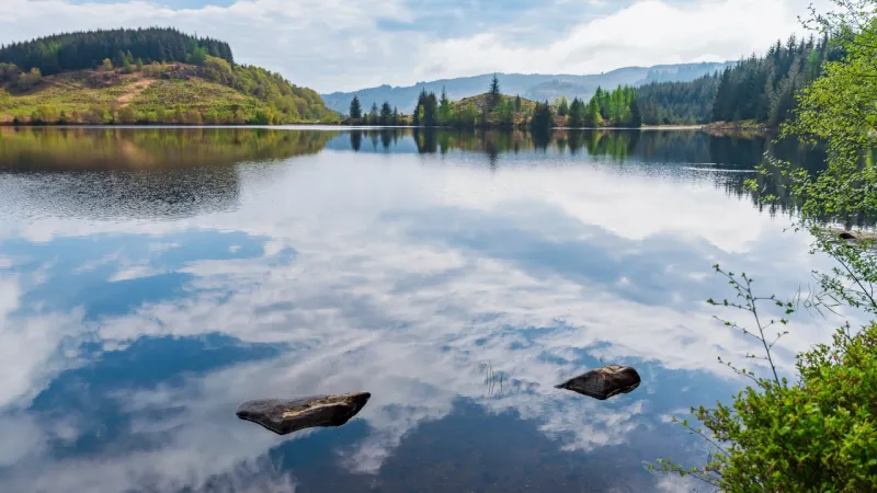 Reservoir surrounded by woodland, with clouds reflected in calm water.