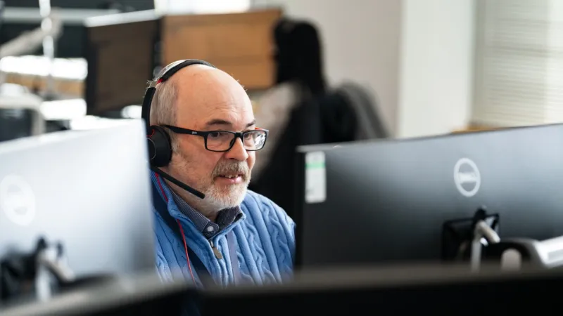 Person wearing a headset and glasses working at a computer in an office environment.