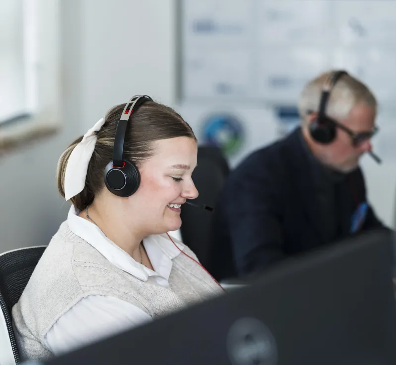 Smiling woman wearing headset in customer service setting with man in background