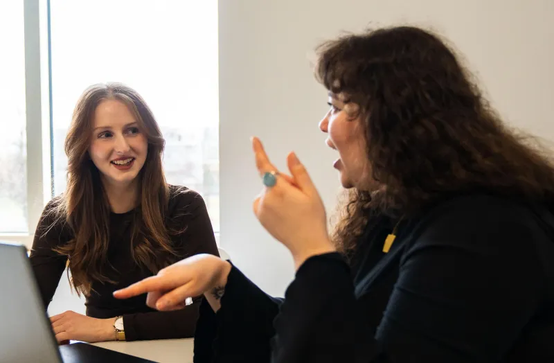 Two women discussing something and gesturing to a laptop screen