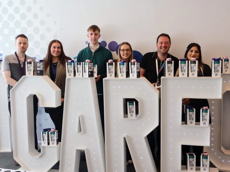 Six colleagues standing behind large floor-standing letters spelling out the world CARE