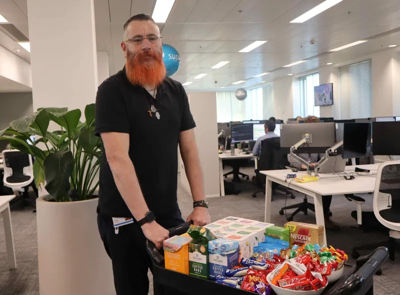 Man pushing trolley containing selection of teas and snacks in office setting